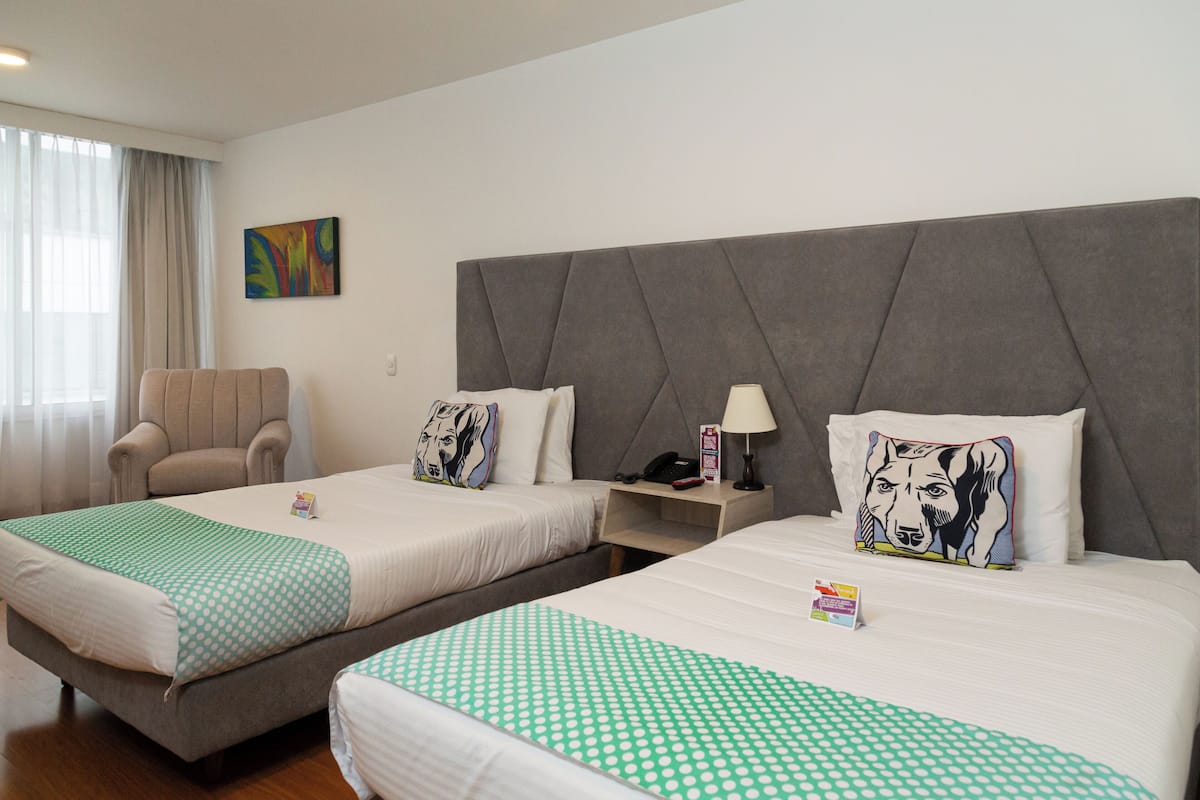 Ein Hotelzimmer mit zwei Betten, einem Sessel, einem Nachttisch und einem Bild an der Wand.