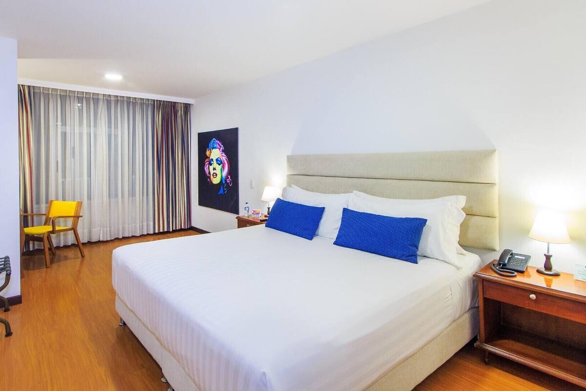 Ein Hotelzimmer mit einem Bett, einem Sessel, einem Schreibtisch mit Telefon und einem Bild an der Wand.