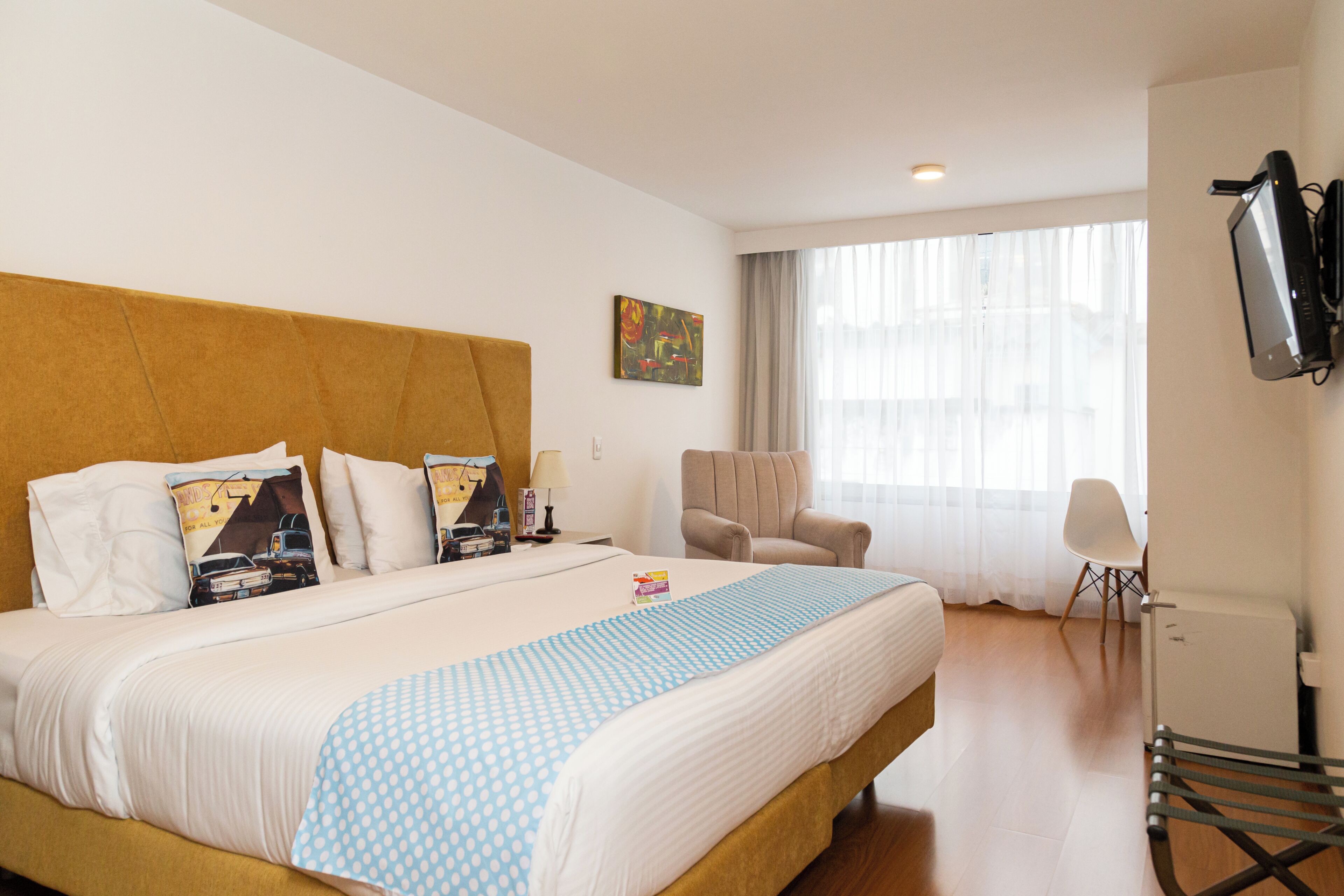 Habitación de hotel con una cama grande, una silla, un escritorio, un televisor y una ventana con cortinas.