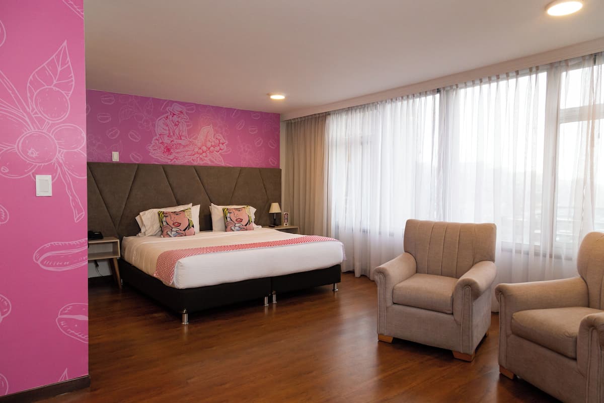 Ein Hotelzimmer mit einem Bett, zwei Sesseln, einem Nachttisch und einer Wand mit floralem Muster.