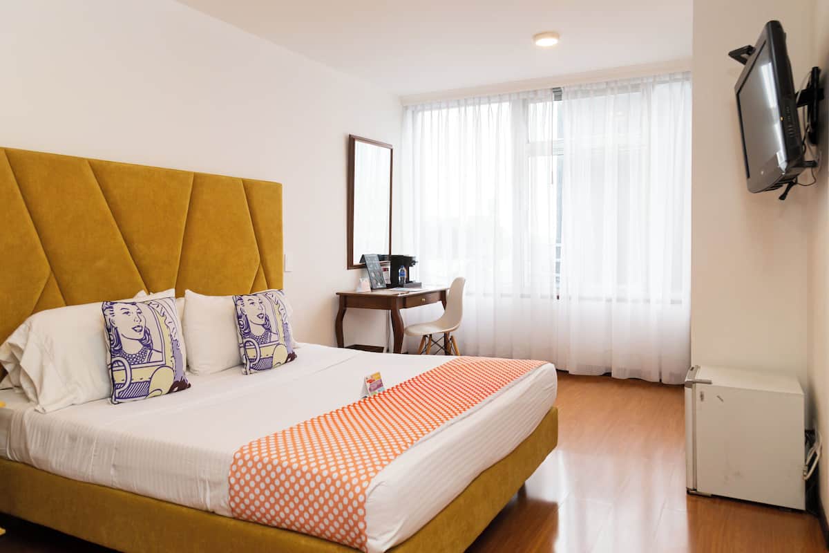 Ein Hotelzimmer mit einem großen Bett, einem Schreibtisch, einem Fernseher und einem kleinen Kühlschrank.