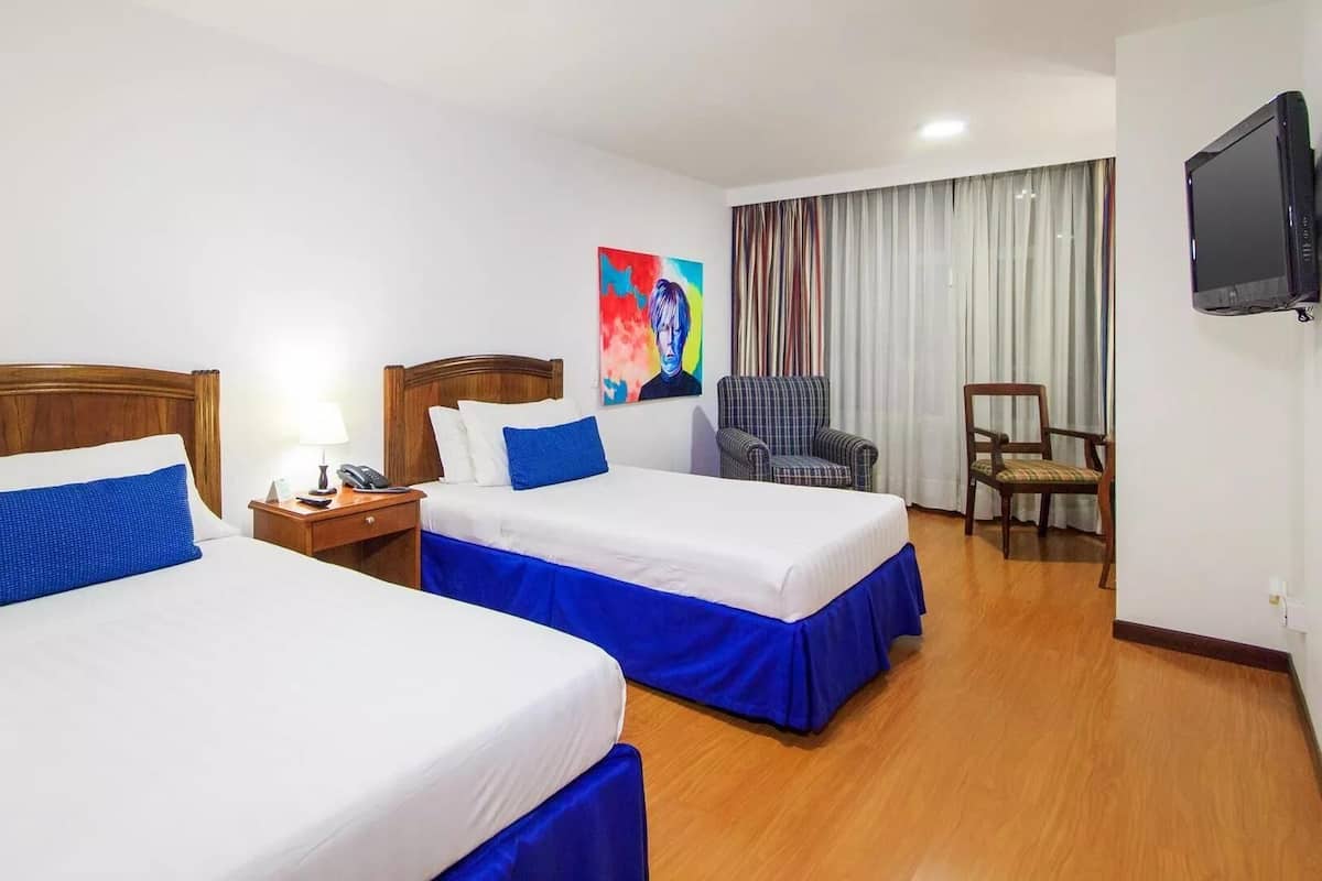 Ein Hotelzimmer mit zwei Betten, einem Fernseher, einem Sessel und einem Bild an der Wand.