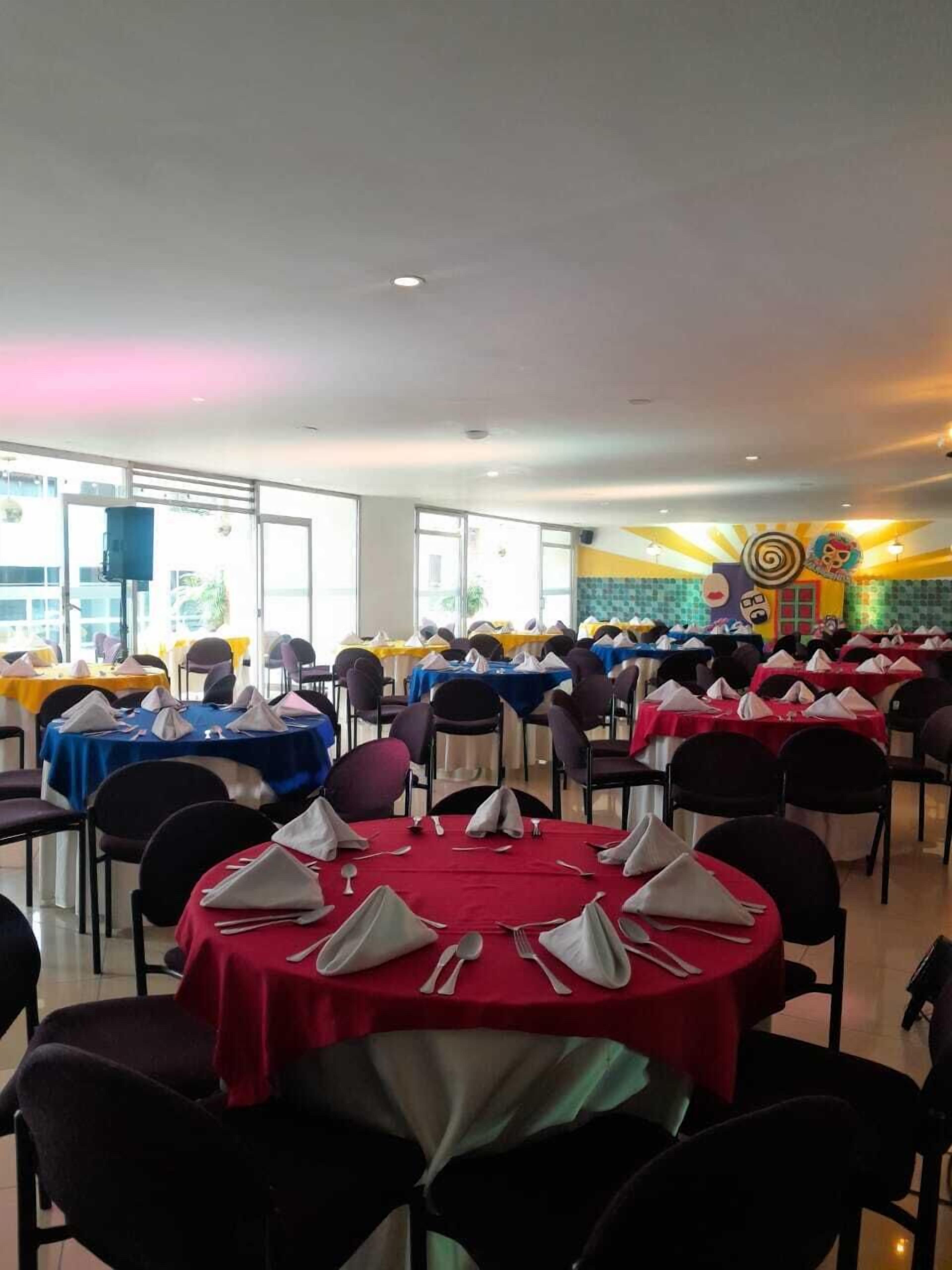 A banquet hall with round tables set for dining, featuring a mix of red and blue tablecloths.