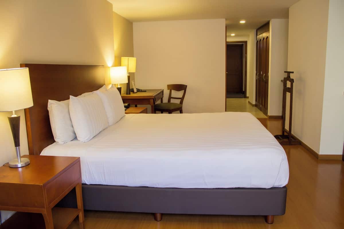 Una habitación de hotel con una cama grande, lámparas de noche, un escritorio y una silla.