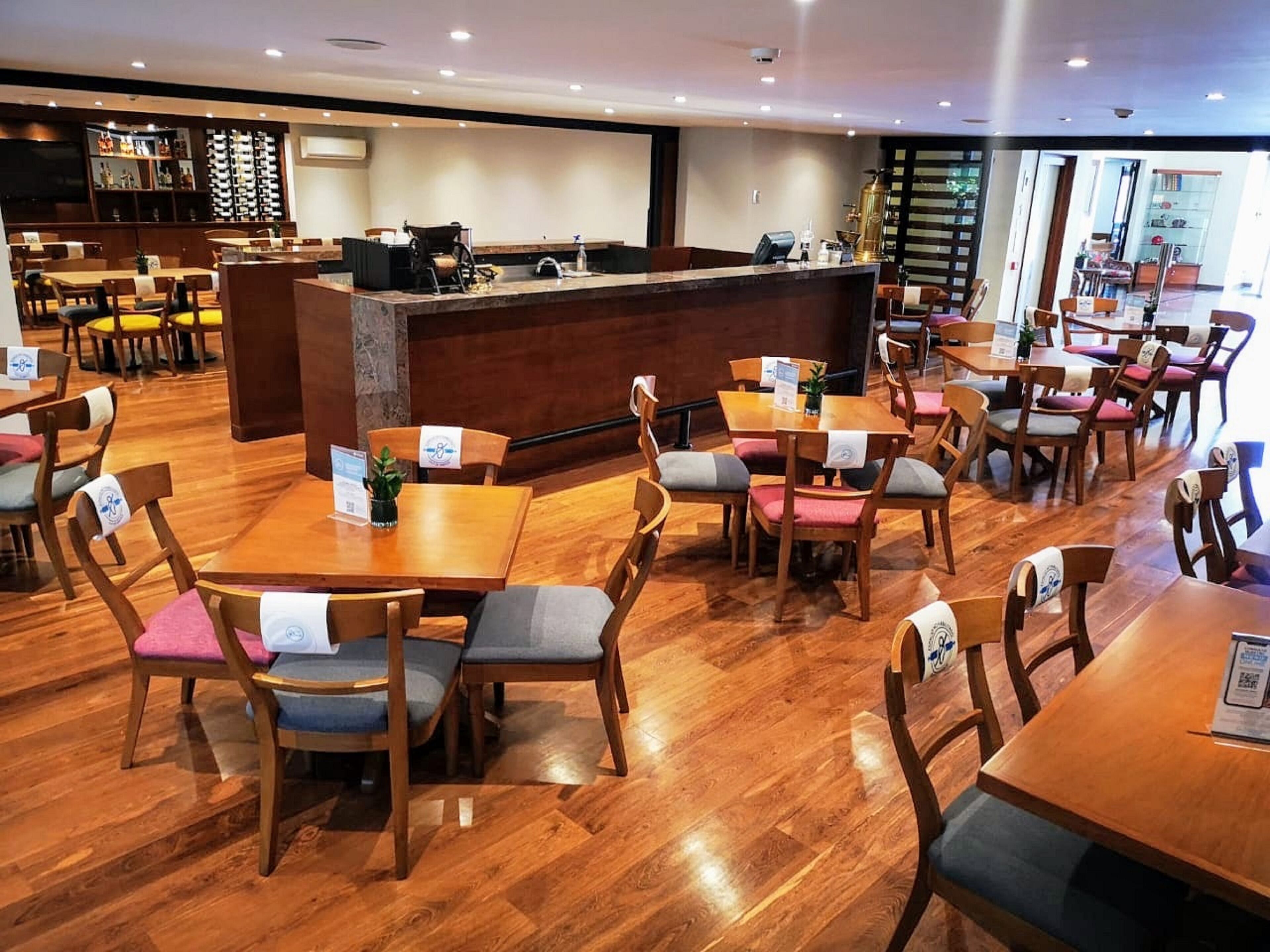 Un restaurante con mesas y sillas de madera, una barra central y una zona de bar al fondo.