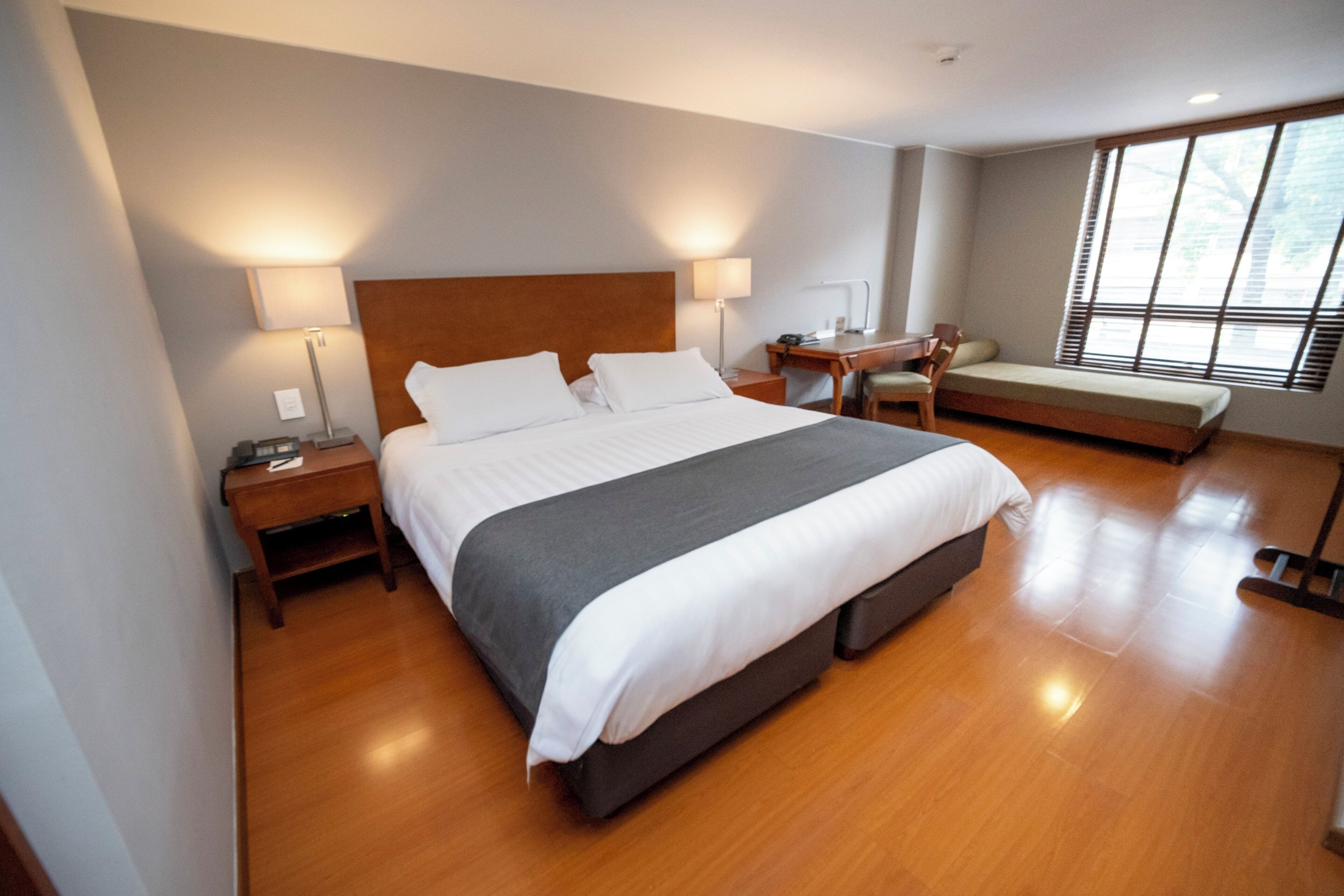 A hotel room with a large bed, bedside tables, a desk, a chair, and a sofa.