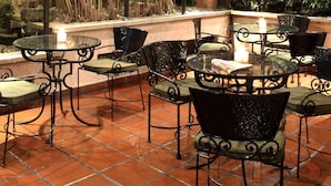 Patio esterno con tavoli e sedie in metallo, immerso nel verde e con pavimento piastrellato.