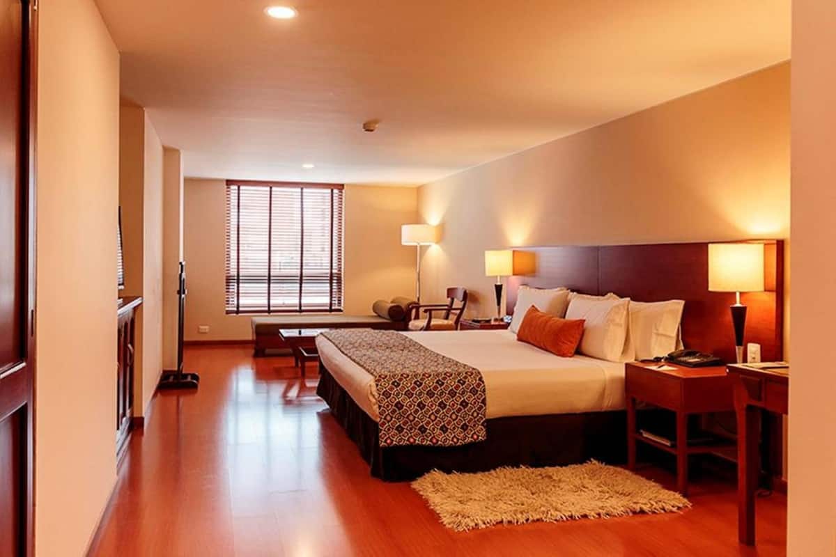 Una habitación de hotel con una cama grande, mesitas de noche, un escritorio y una ventana con persianas.