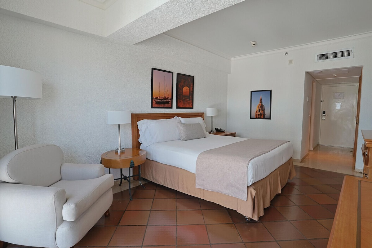 Een hotelkamer met een bed, twee nachtkastjes, een stoel en kunstwerken aan de muur.