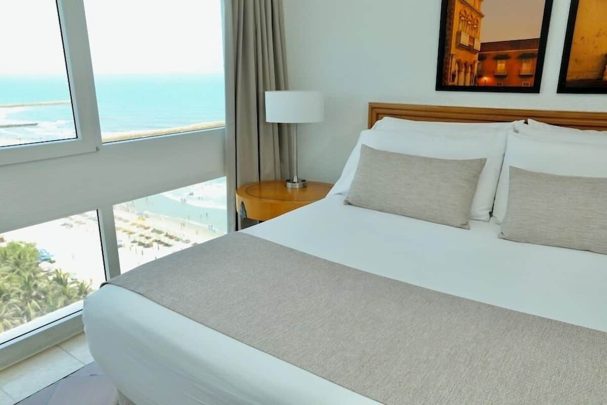 Een hotelkamer met een groot bed, een nachtkastje met lamp en uitzicht op de oceaan.
