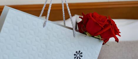 A hand holding a light blue gift bag with a geometric pattern and a black floral design, containing a red rose.