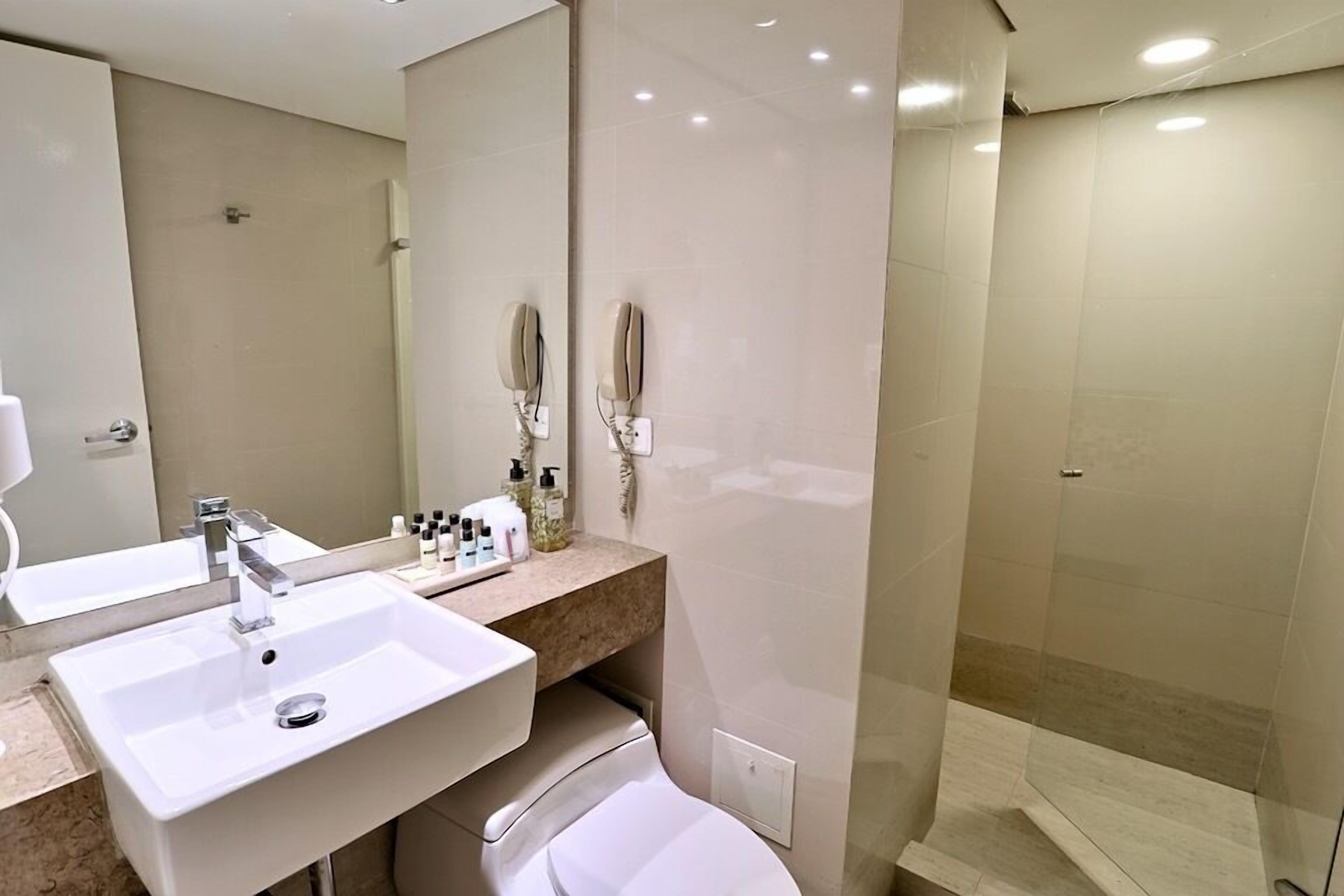 A modern bathroom with two sinks, a mirror, a toilet, and a glass-enclosed shower.