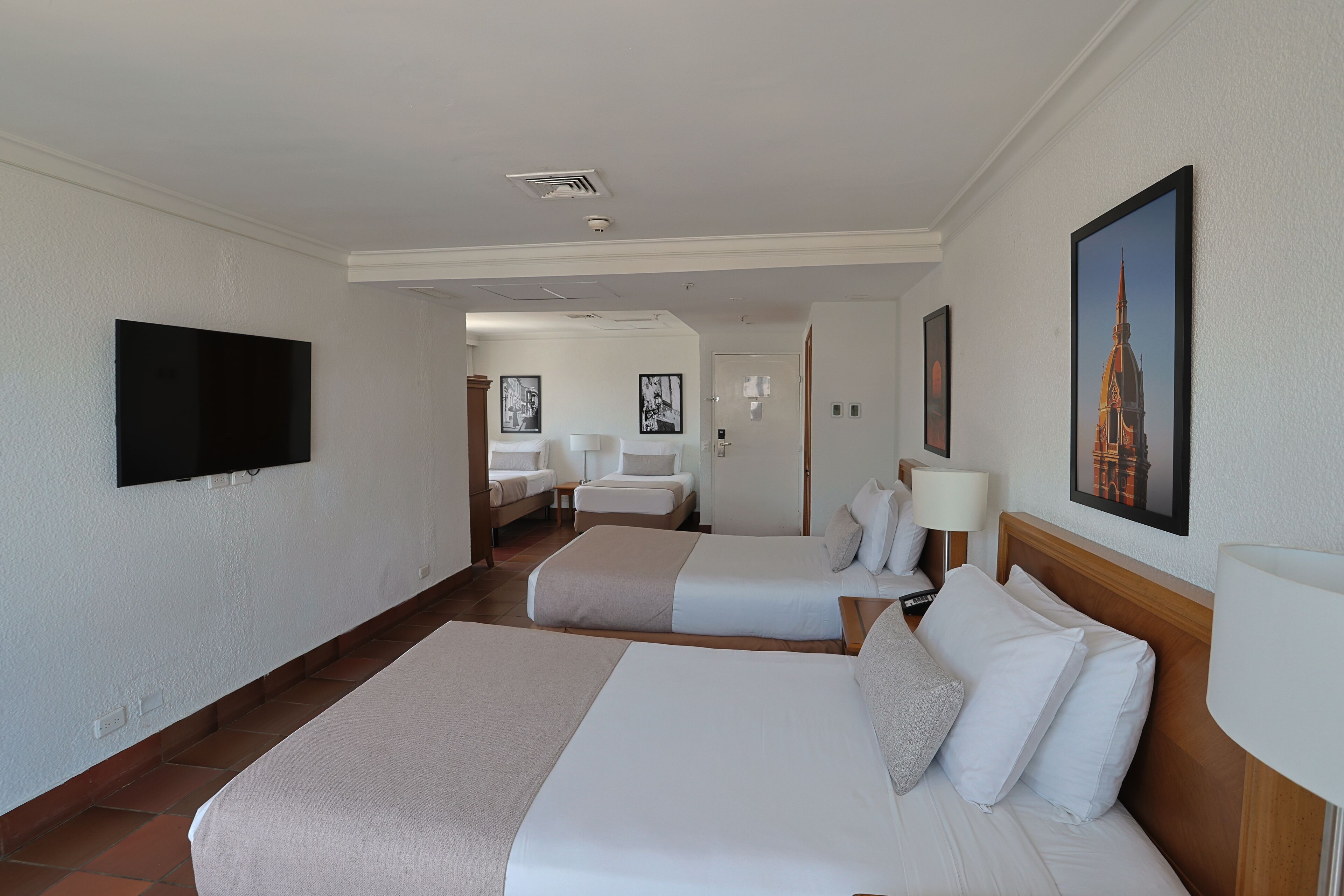 A hotel room with two beds, a flat-screen TV mounted on the wall, and a framed picture of a building.