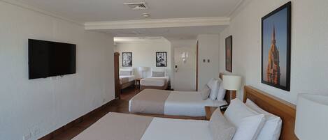 A hotel room with two beds, a flat-screen TV mounted on the wall, and a framed picture of a building.