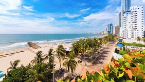 Una playa con palmeras, orilla de arena y un horizonte urbano con edificios altos.
