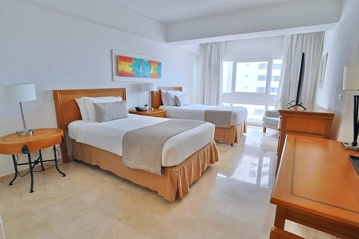Een hotelkamer met twee bedden, een bureau, een stoel, een lamp en een schilderij aan de muur.