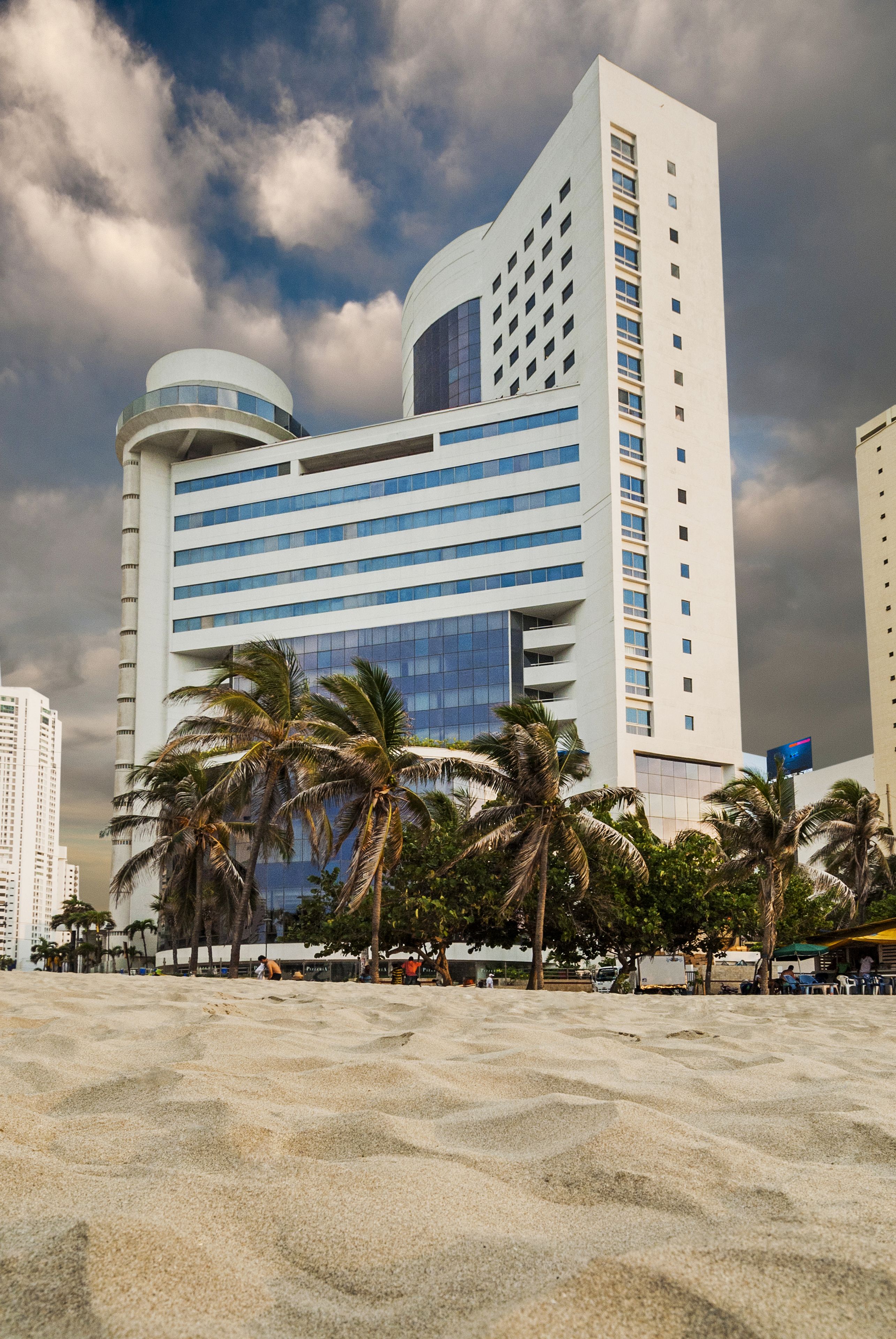 A modern hotel with a curved facade, multiple floors, and a prominent cylindrical structure at the base.