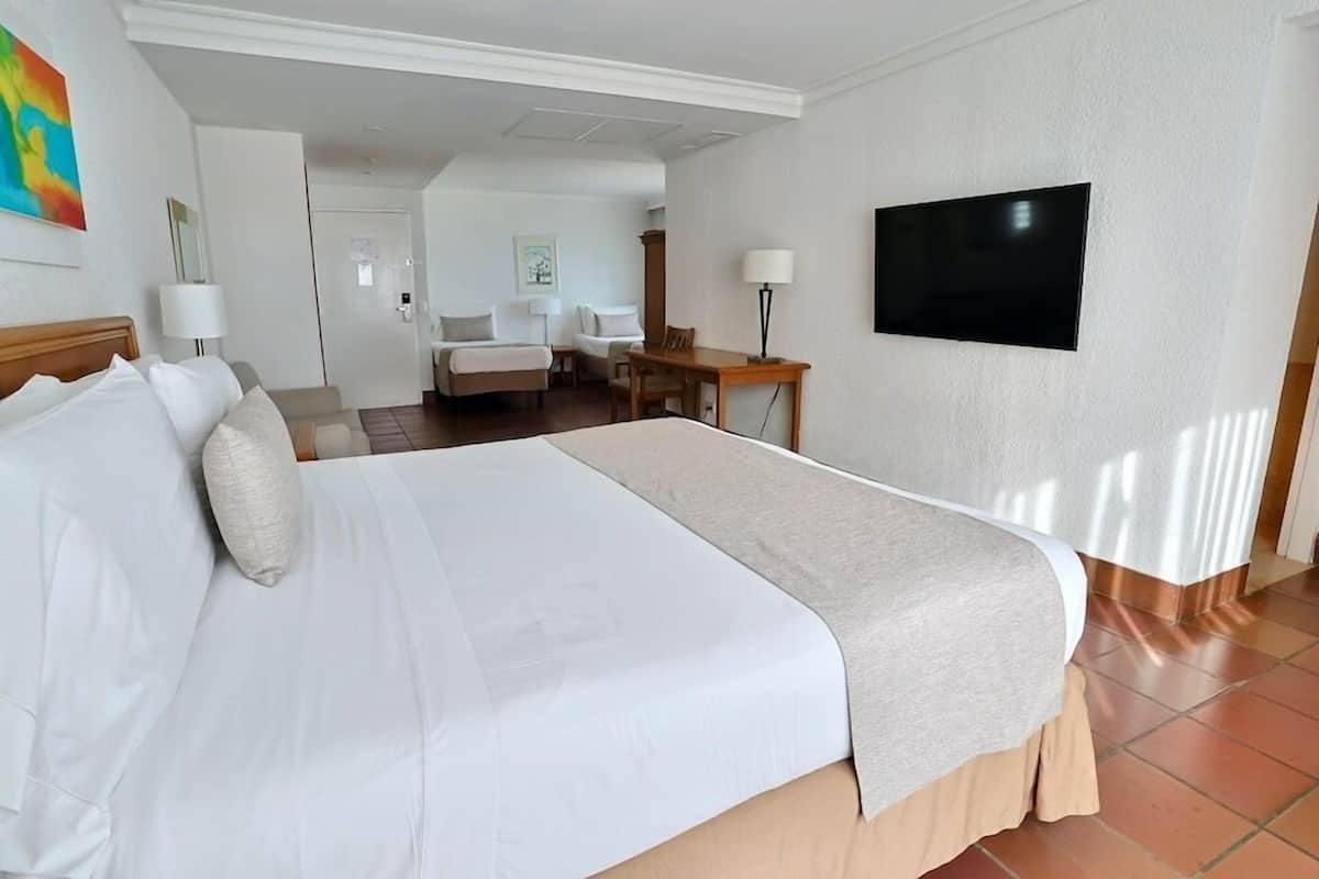 Een hotelkamer met een groot bed, een bureau, een stoel, een televisie en een deur naar een andere kamer.