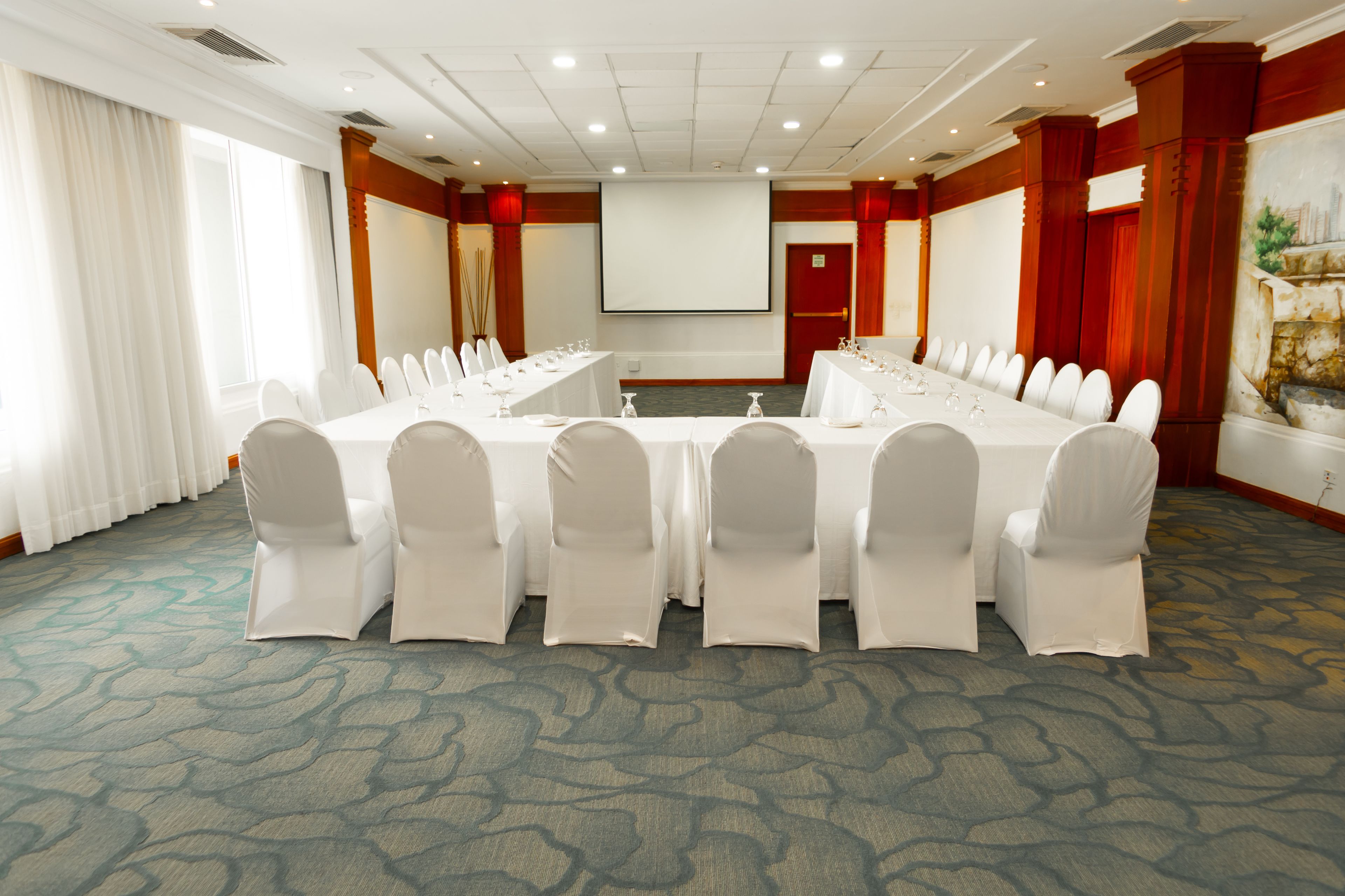 A conference room with a long table, white chairs, a projector screen, and a carpeted floor.