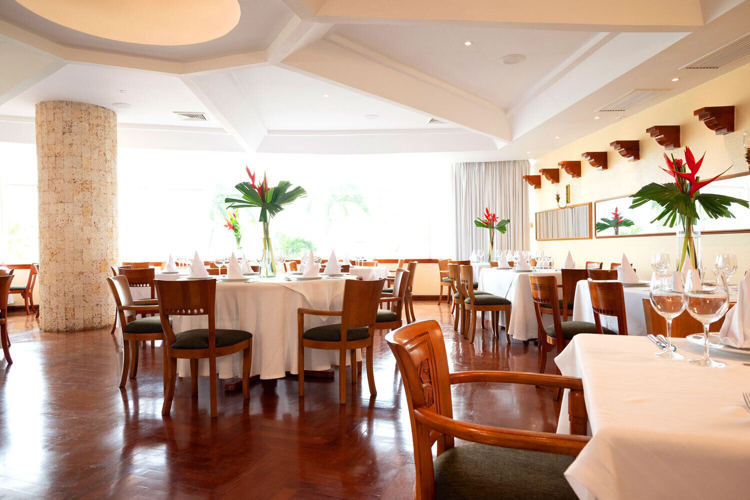 A spacious dining area with round tables, wooden chairs, and a large pillar.