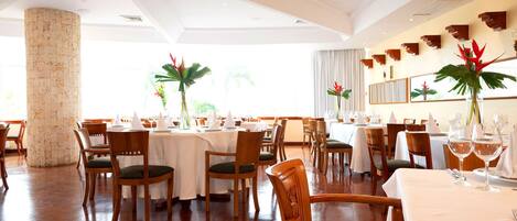 A spacious dining area with round tables, wooden chairs, and a large pillar.