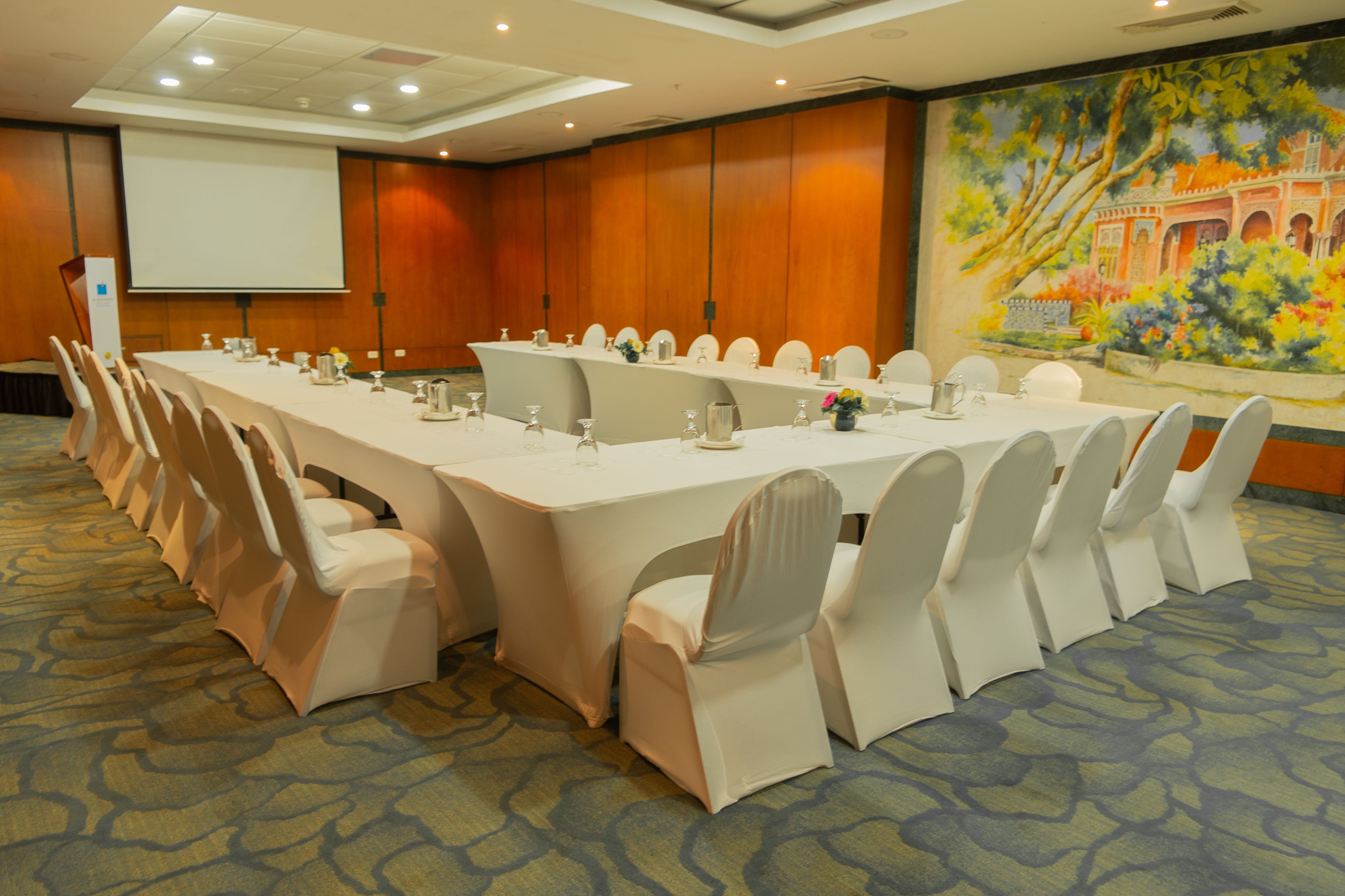 A conference room with a long table, white chairs, and a projector screen.