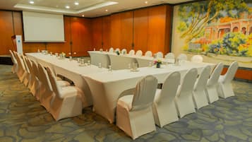 A conference room with a long table, white chairs, and a projector screen.