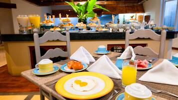 Un bufé de desayuno con diversas opciones de comida y bebidas, que incluye un plato de huevos, pasteles y un vaso de jugo de naranja.