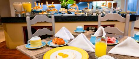 A breakfast buffet with various food items and drinks, including a plate of eggs, pastries, and a glass of orange juice.