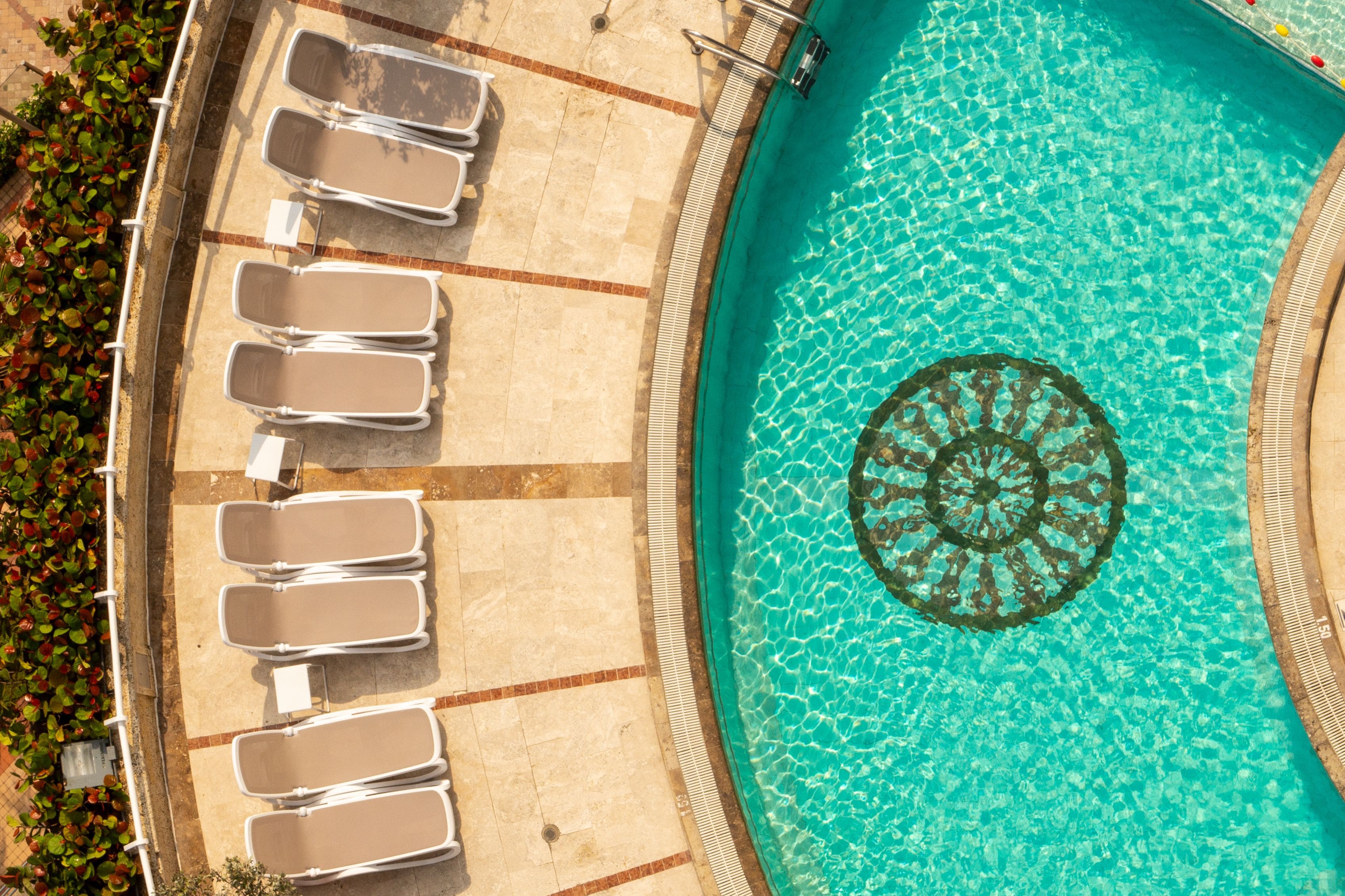 An aerial view of a swimming pool with sun loungers and a decorative fountain.