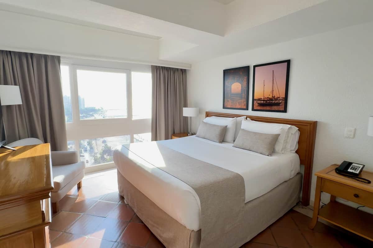 Een hotelkamer met een bed, een bureau, een televisie, een nachtkastje en een raam met gordijnen.