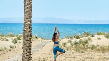 Una persona practicando yoga en una playa arenosa con una palmera y una vista despejada del océano.