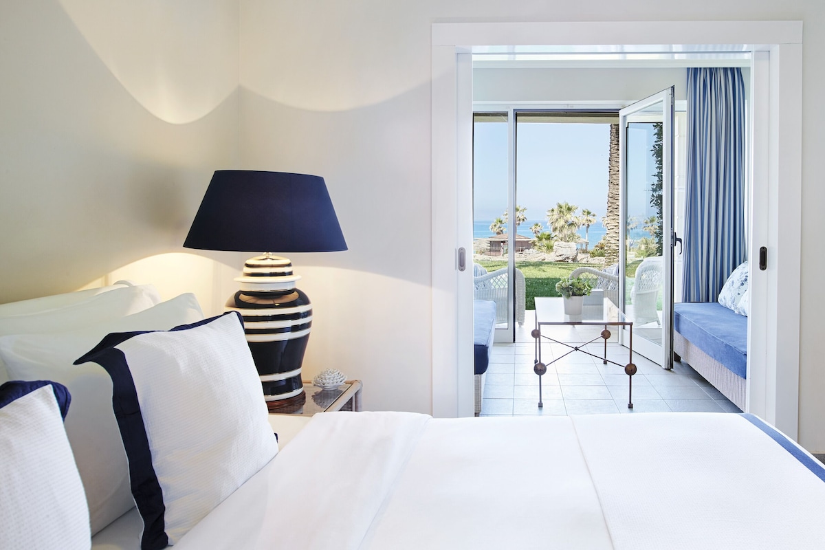 A hotel room with a bed, a lamp, a table, and a view of the outdoors.