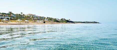 A coastal area with clear water, beach umbrellas, and buildings in the background.