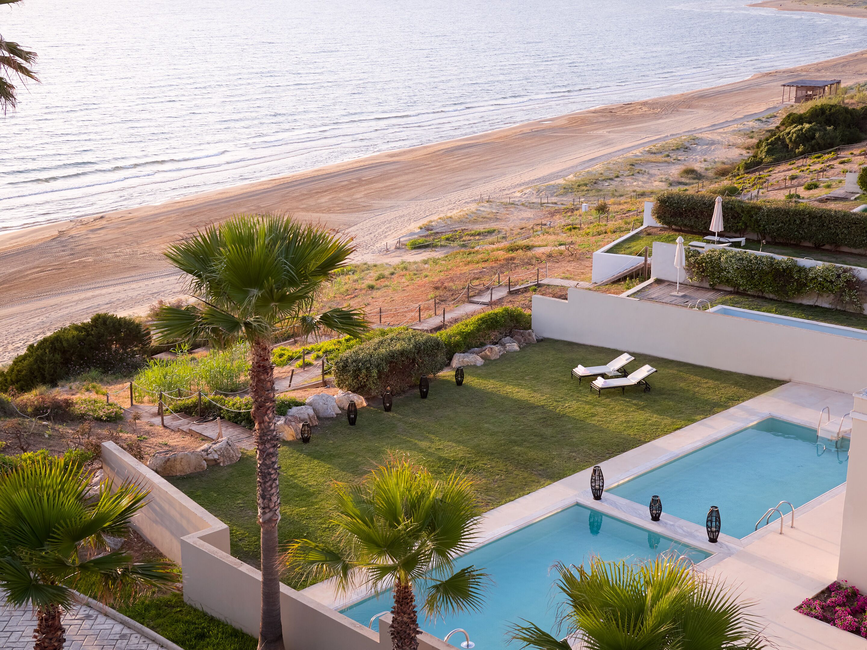 A pool area with lounge chairs, a small pool, and a view of the beach.