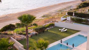 A pool area with lounge chairs, a small pool, and a view of the beach.