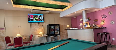 Een pooltafel met ballen, een televisie en een bar met een bord waarop 'Coffee Bar' staat.