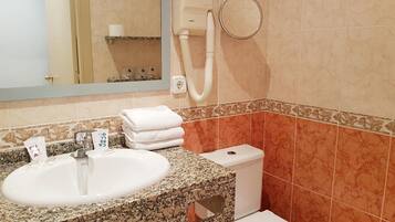 A bathroom with a sink, mirror, towel stack, and toilet.