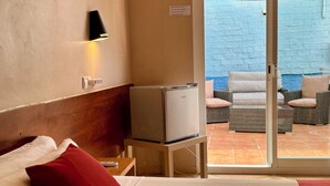 A hotel room with a bed, a TV on a stand, a wall-mounted air conditioner, a small table with a remote control, and a sliding glass door leading to an outdoor seating area with chairs. - Hotel Piccadilly Sitges (Sitges)