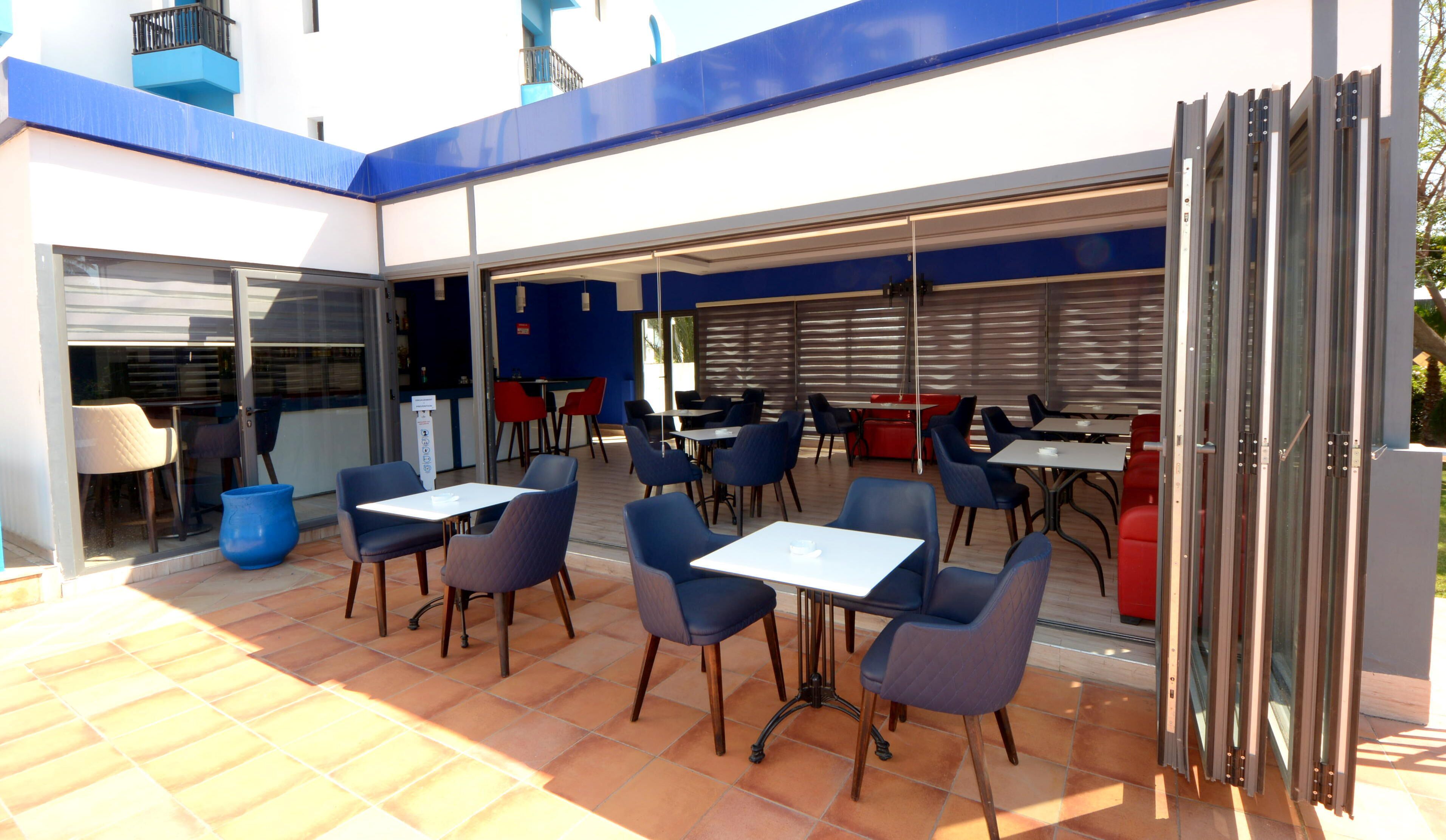 An outdoor patio area with multiple tables and chairs, a glass door entrance, and a blue and white building facade.