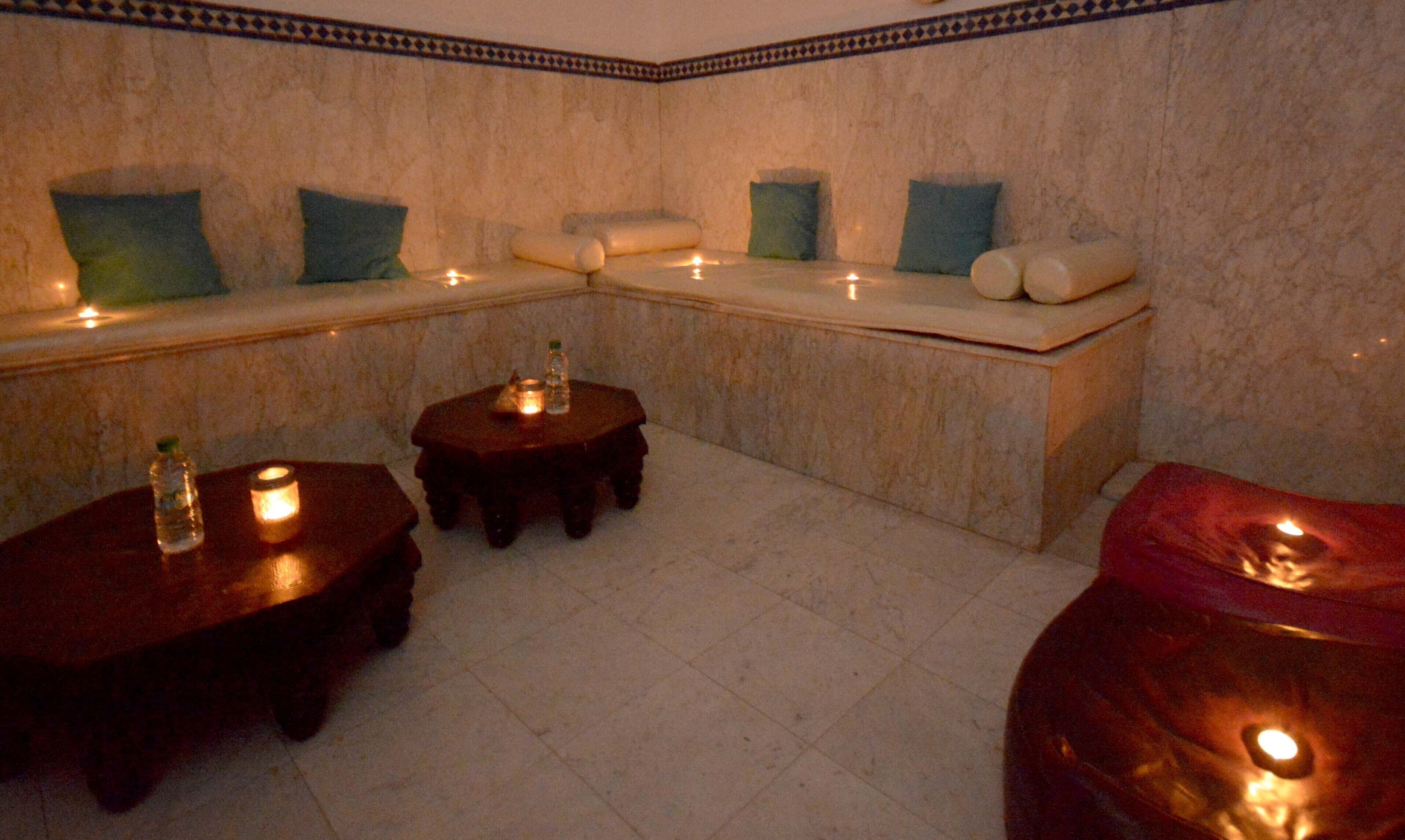 Un cuarto de spa con piso de mármol, una zona de descanso con cojines y mesitas con velas.