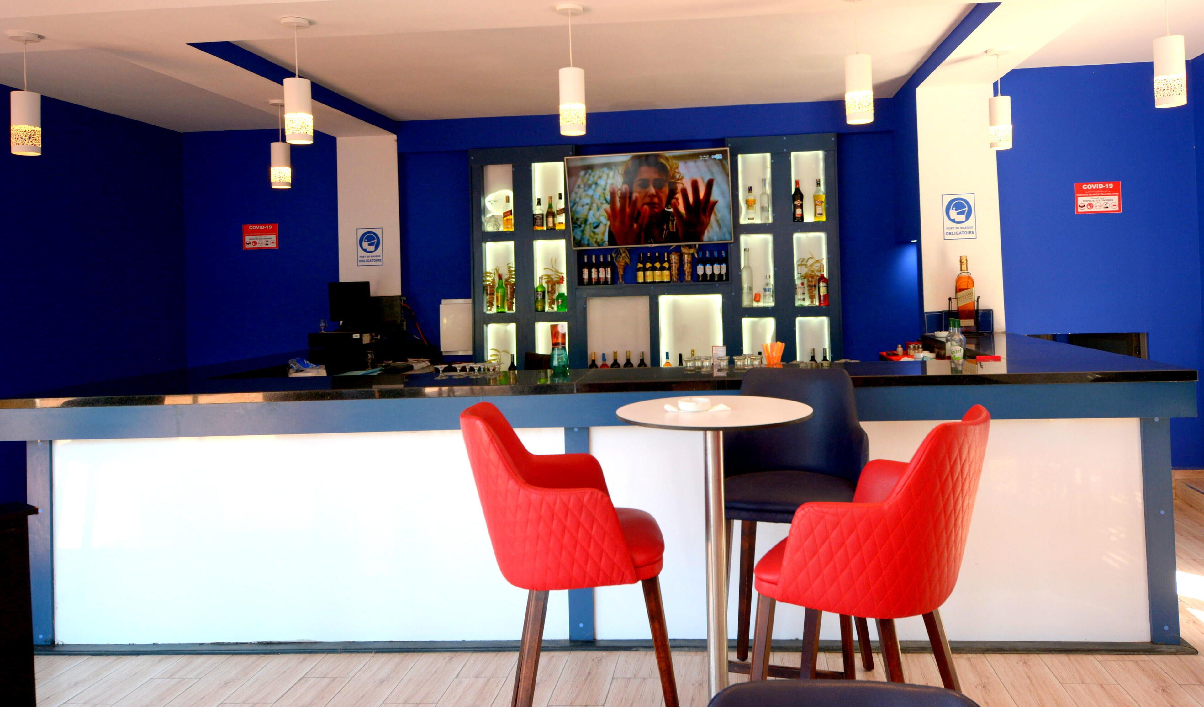 Eine Bar mit blau-weißer Farbgebung, ausgestattet mit einer Theke, zwei roten Sesseln und einer Auswahl an Flaschen.