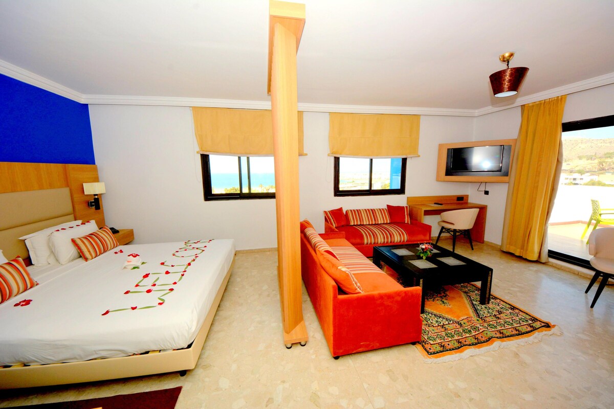 A hotel room with a bed, a sofa, a desk, a TV, and a view of the outdoors.