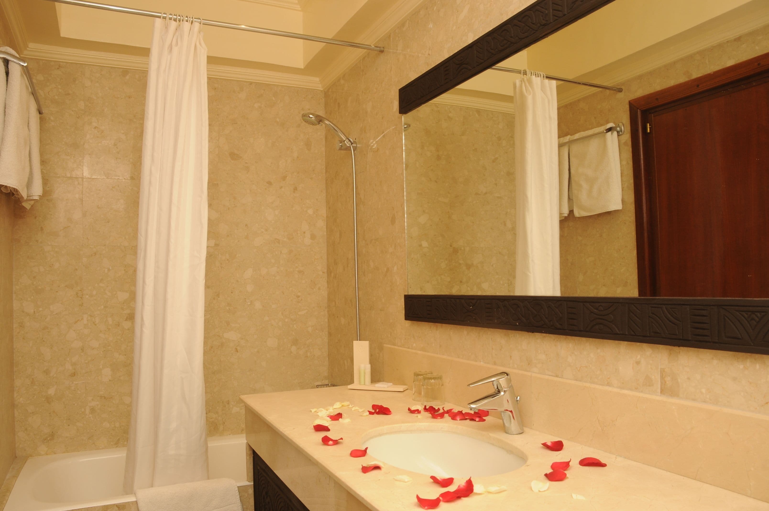 Un bagno con vasca, doccia, lavandino con petali di rosa e specchio.