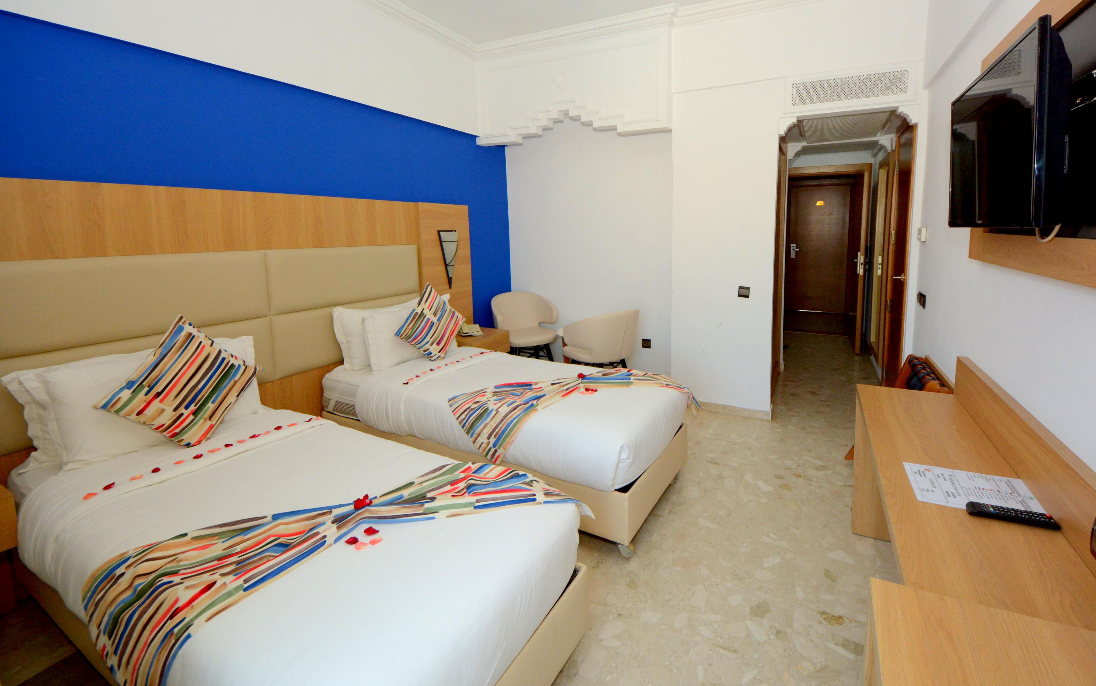 Habitación de hotel con dos camas, televisor, escritorio y una silla.