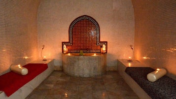 Relax in a serene space with a stone bench and candles, surrounded by arched walls and a tiled floor.