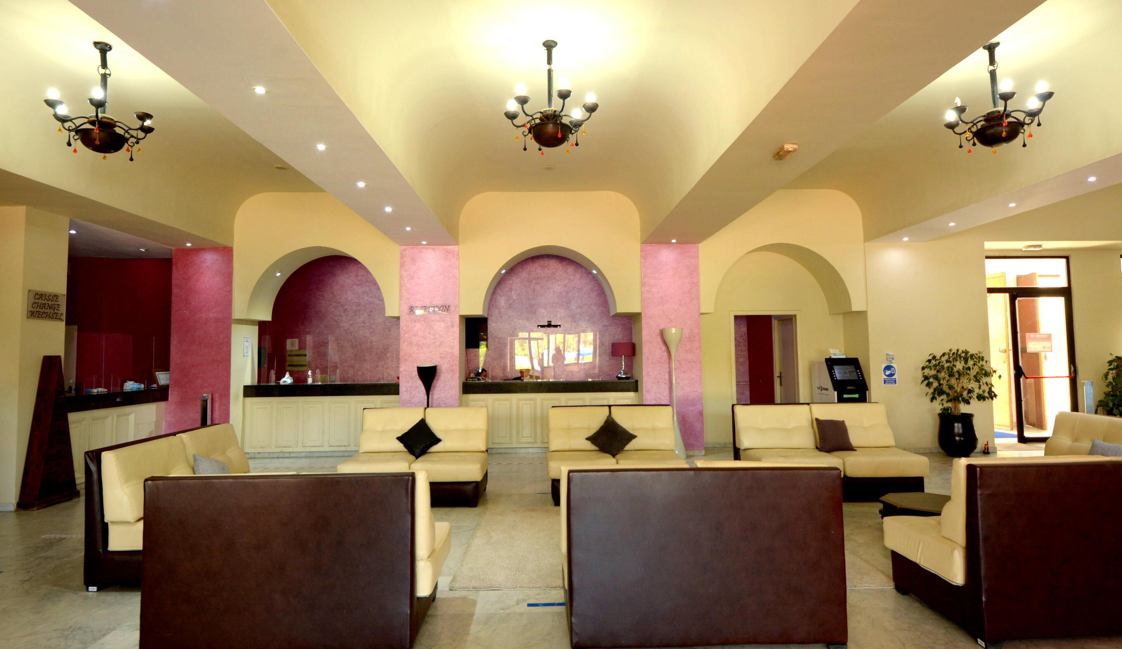 Un vestíbulo de hotel con mostrador de recepción, varias zonas de estar y candelabros.