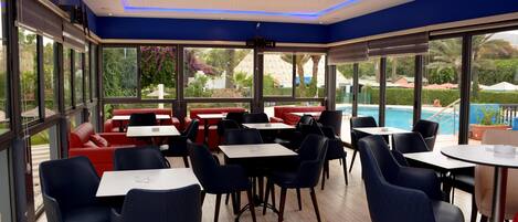 A modern indoor dining area with large windows, red seating, and a pool view.
