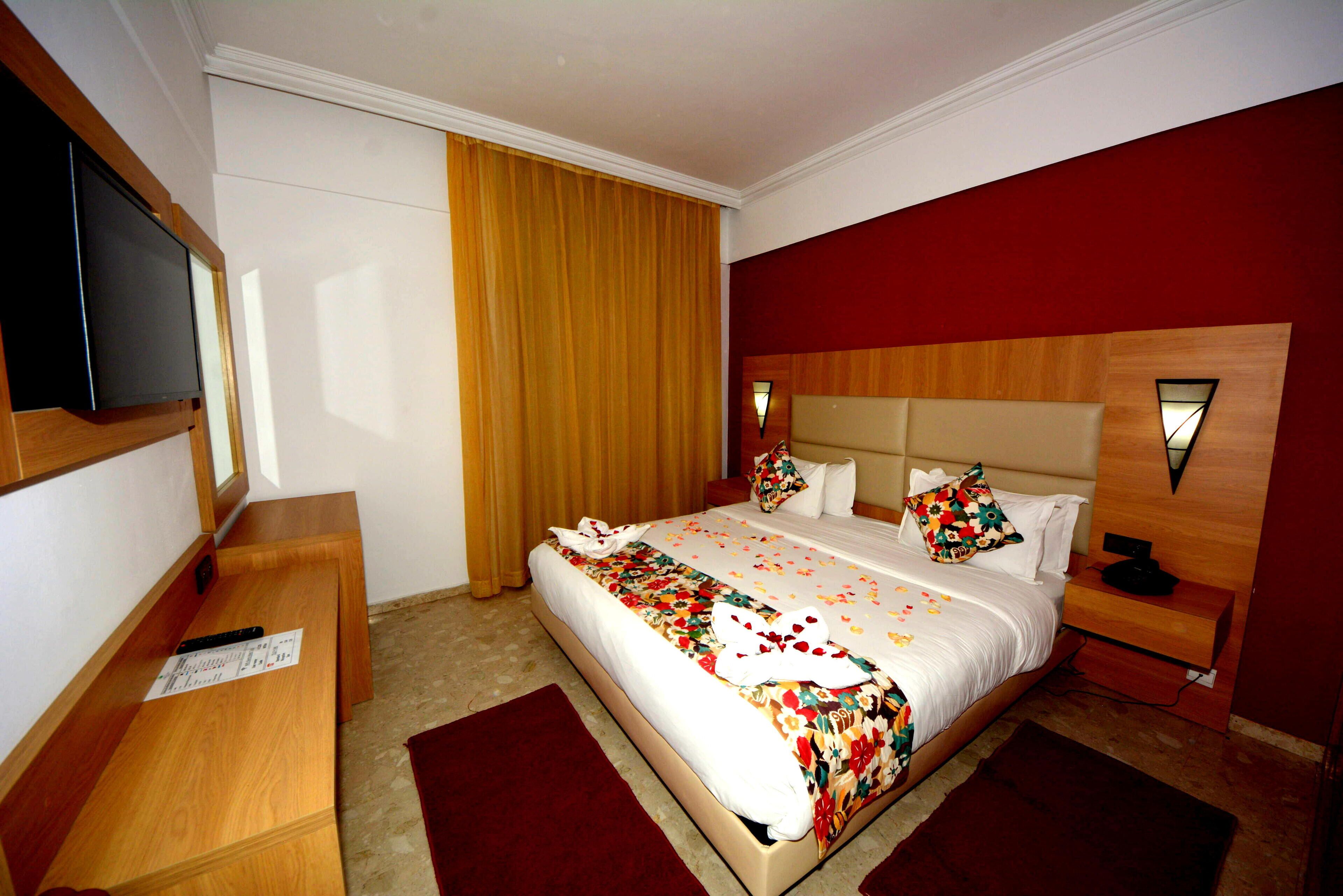 A hotel room with a large bed, a television on a wooden stand, a wooden headboard, and a red accent wall.