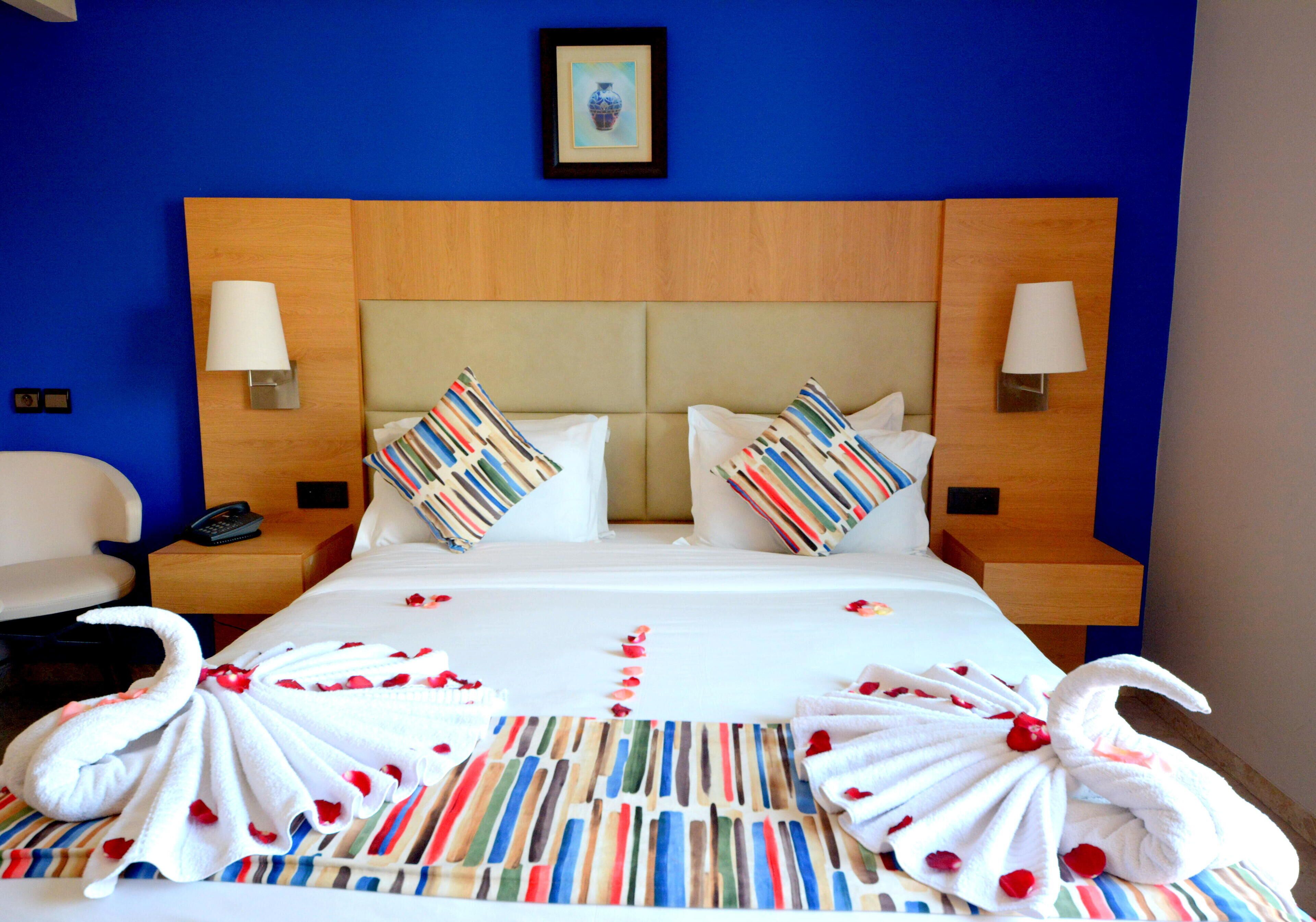 A hotel room with a large bed, two pillows, a headboard, bedside lamps, a telephone, and a framed picture on the wall.